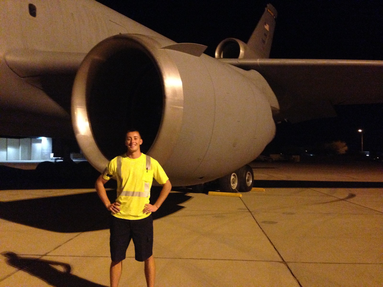 Standing on the ramp at night in a high visibility shirt beside the engine of a military widebody aircraft, chocks set under the main gear