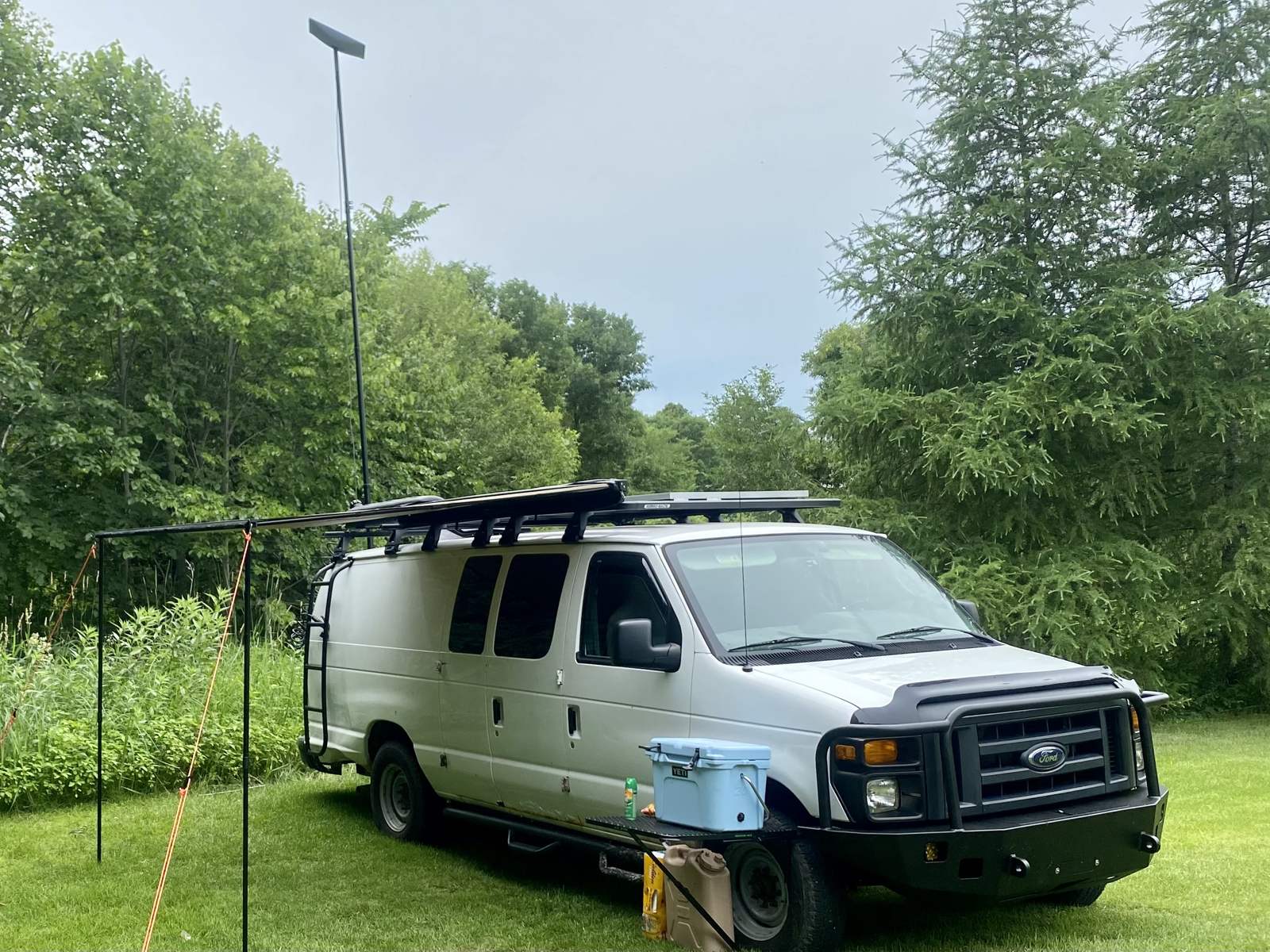 The van on grass with the side awning staked out and the Starlink dish raised high on a mast above the roof rack