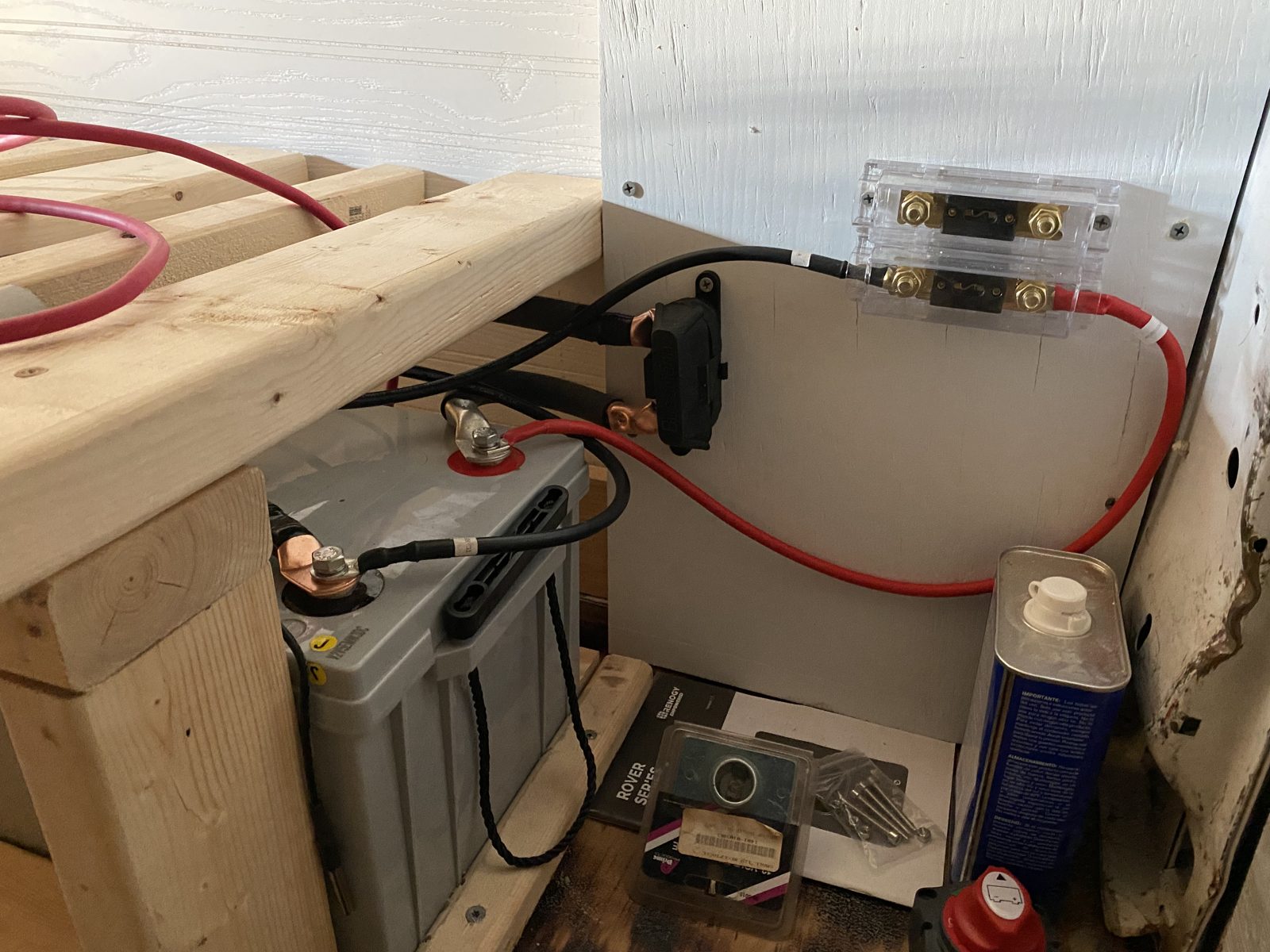 The battery bank inside the van, with lugged cable runs, an inline fuse holder and a clear ANL fuse block mounted to the wall above it